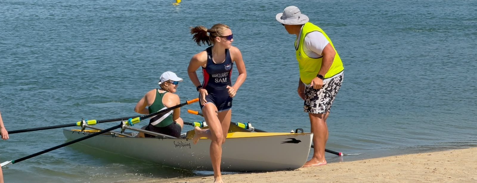 Alia Marquardt leaping from the coastal double at the water's edge while her partner steadies the boat